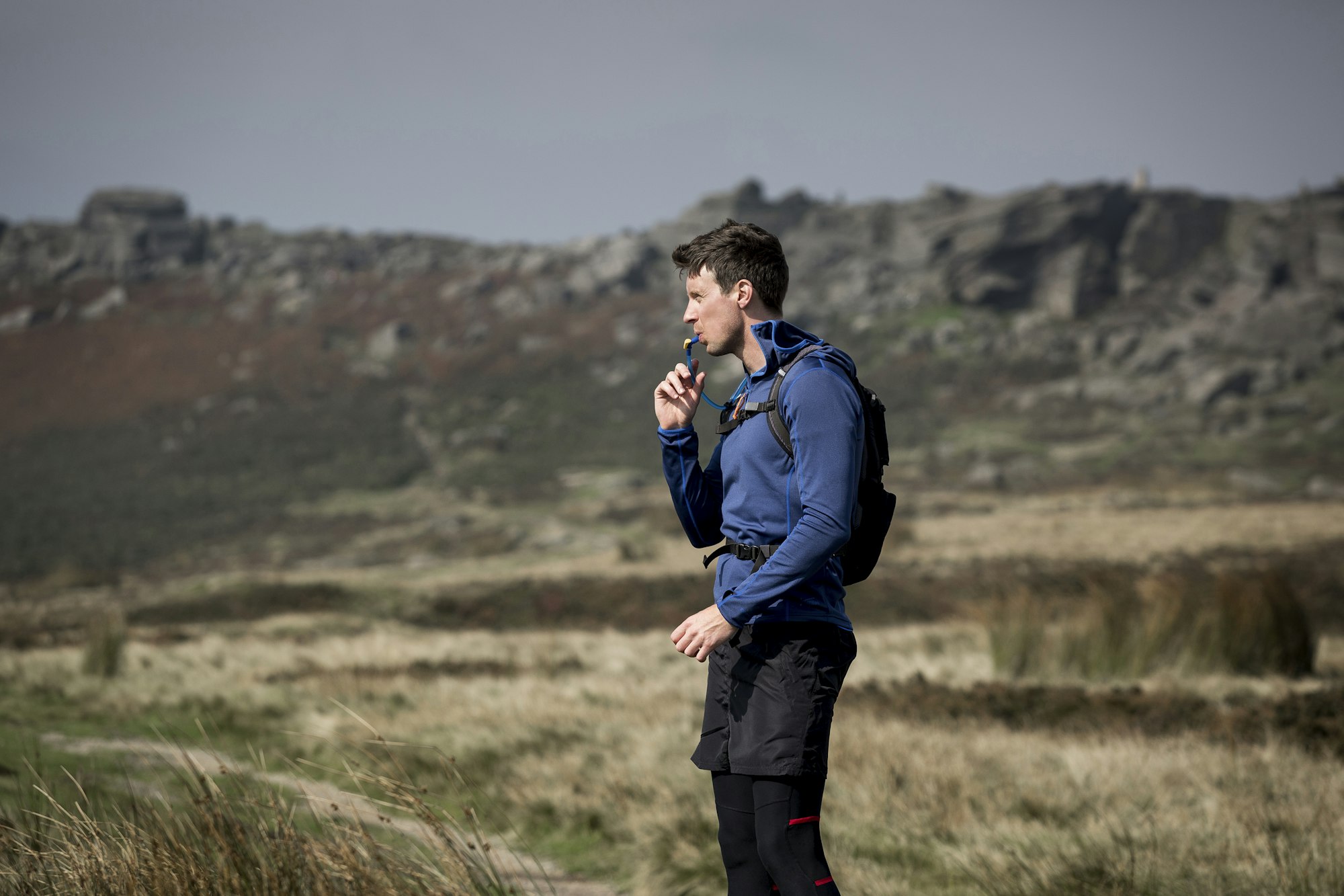 Male runner drinking from tube at Stanage Edge, Peak District, Derbyshire, UK